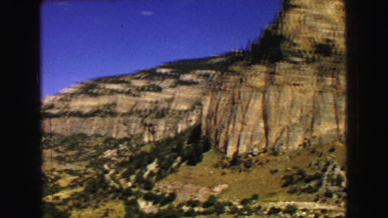 Closer view of a tall rock wall and sloping terrain beneath blue sky.