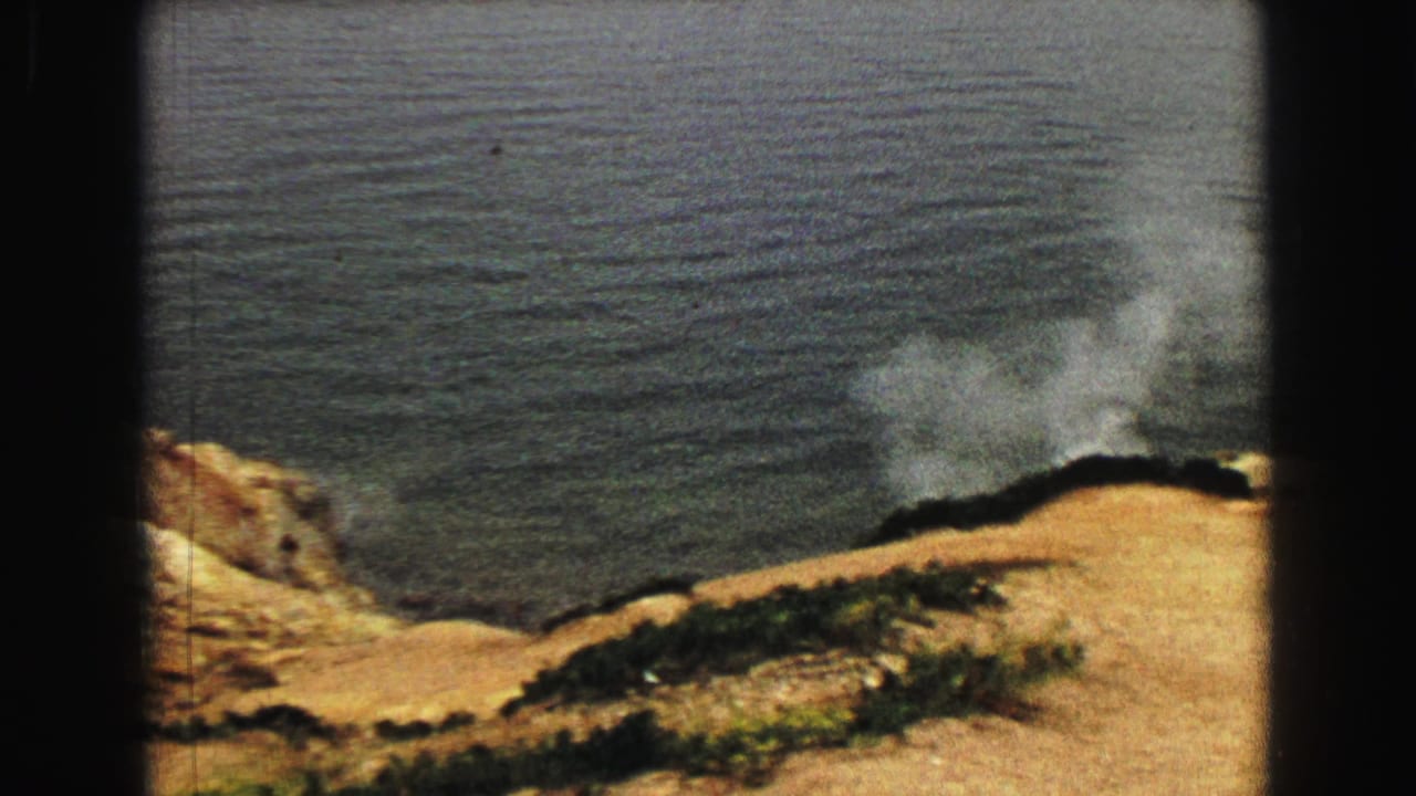 A steam plume rises along the edge of a tan hillside beside the lake.