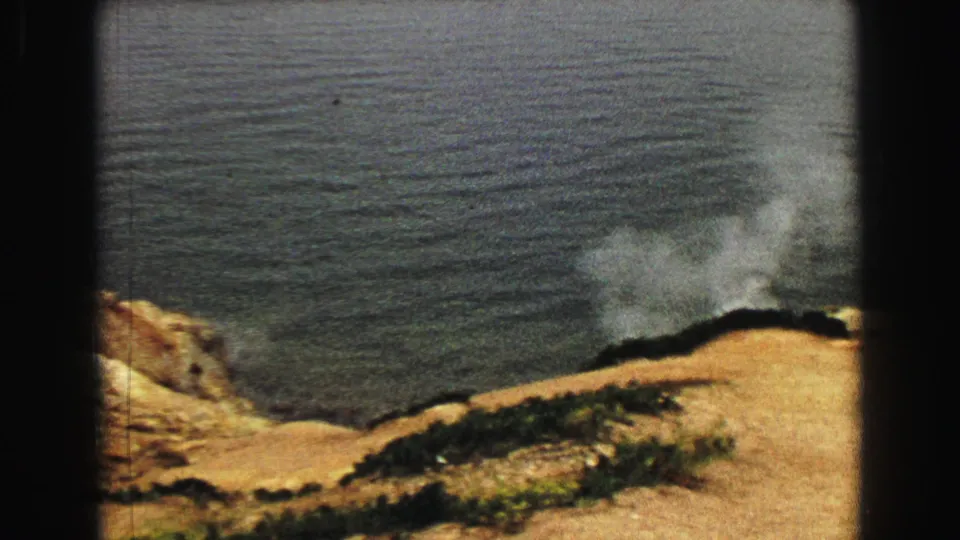 1967 Yellowstone 8mm frame of steam lifting from a rocky tan slope at the edge of a dark lake.
