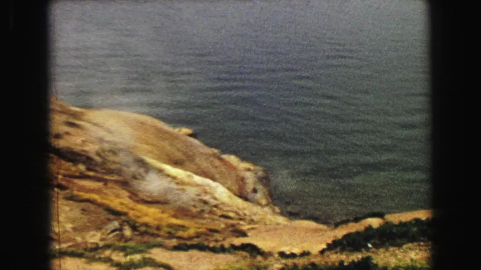 1967 Yellowstone 8mm frame looking down across a rocky dirt hillside toward greenish lake water.