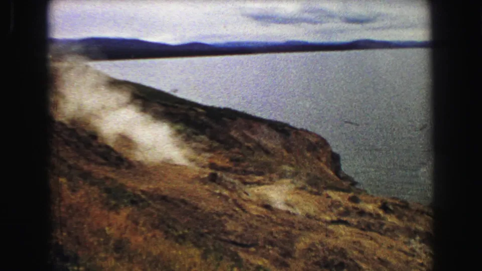 Yellowstone, Wyoming 8mm frame from 1967 with steam spreading across a rugged slope near a large lake or river.
