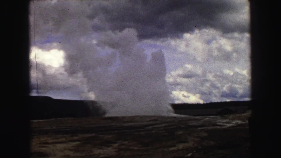 The Old Faithful plume expands across the lower frame, with Yellowstone terrain and cloud cover visible in 1967 8mm home-movie footage.
