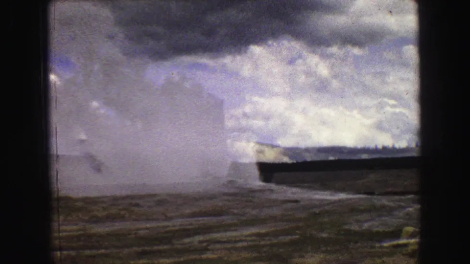 A wider 1967 Yellowstone view shows Old Faithful's steam plume over textured ground, framed by dark 8mm film edges and cloudy sky.