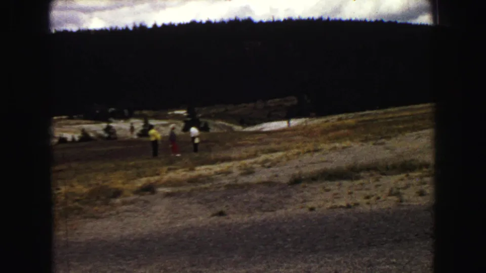 Distant visitors in Yellowstone watch from a hillside near geothermal ground, captured in a 1967 home-movie frame.