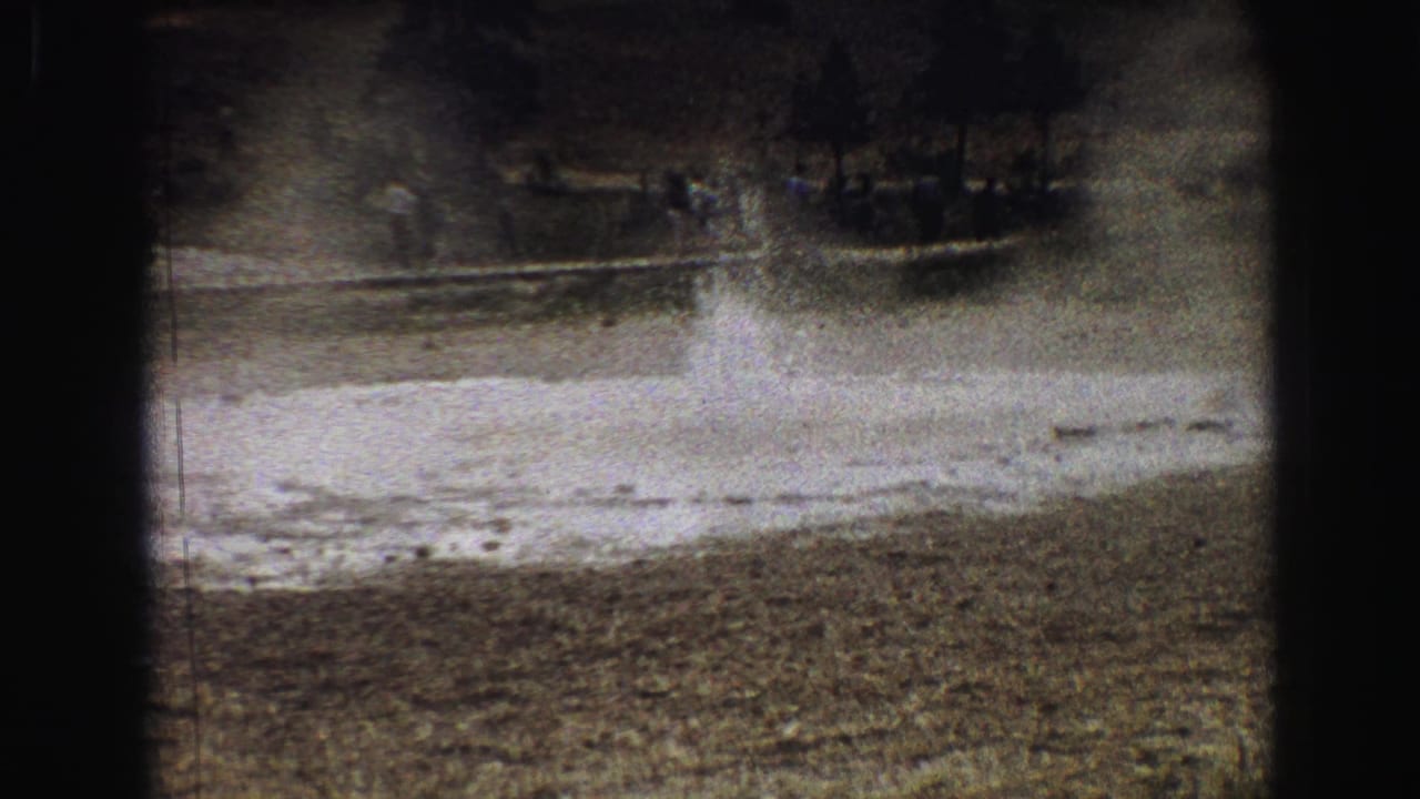 Geyser spray continues above a rough vent with people visible across the background.