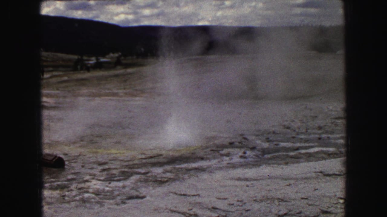 Steam rises from a geyser field below distant dark hills.