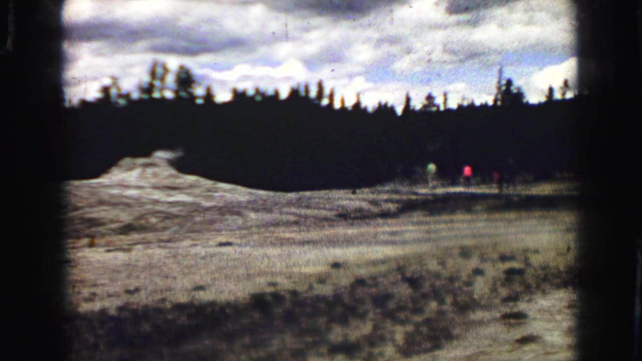 Geyser mound and thermal ground with small distant visitors near the right edge.