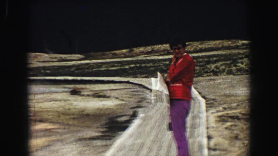 Yellowstone 1967 8mm frame showing a visitor at the boardwalk rail near pale mineral deposits and distant steam.