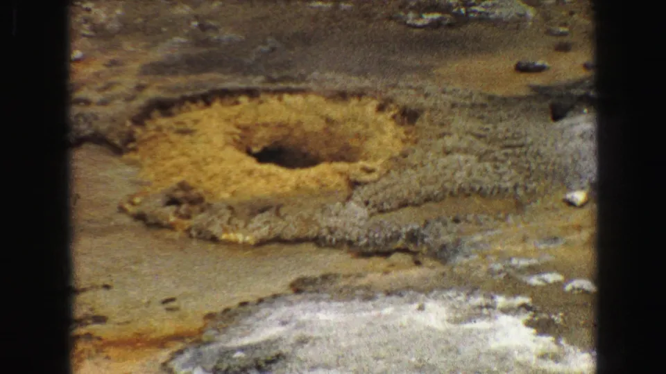 Close Yellowstone 8mm view of a yellow-rimmed hot spring or mineral pool surrounded by textured geothermal deposits.