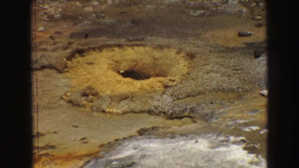 1967 Yellowstone home-movie frame focused on a yellow mineral pool and pale geothermal surface with visible 8mm frame edges.