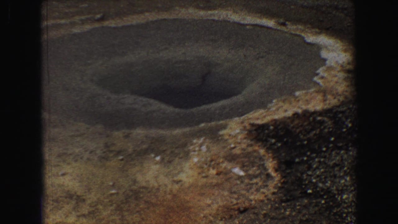 Mineral-edged geothermal opening in barren ground with dark 8mm frame borders.