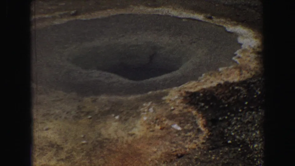 1967 Yellowstone 8mm frame showing a dark geothermal opening surrounded by pale mineral deposits and rough earth.