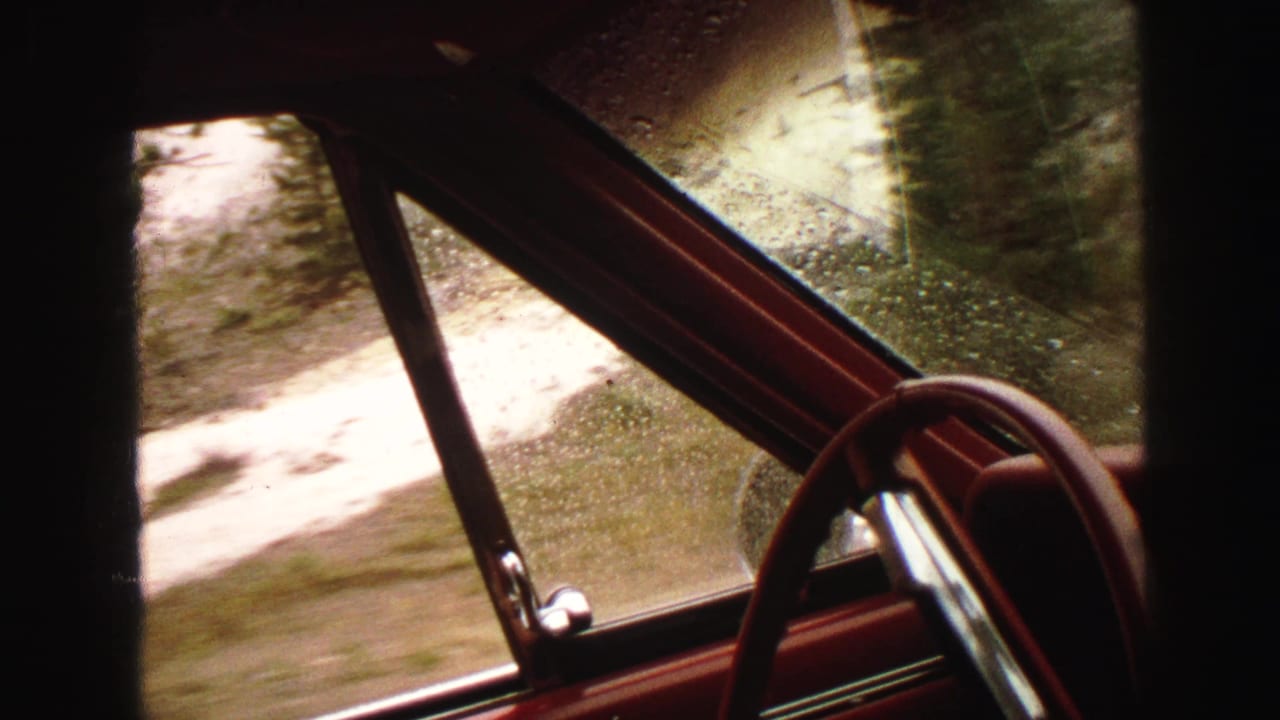 Passenger-side view through a rainy car window with a red door frame and steering wheel visible.