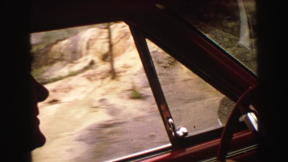A driver profile is visible in the 1967 Yellowstone home-movie footage as the car moves past a wet dirt road and trees.