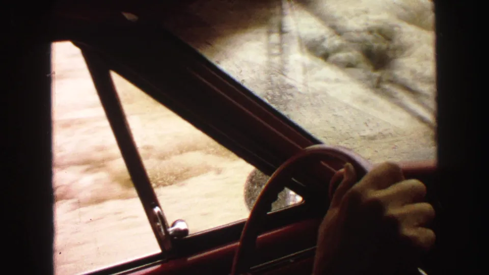 Yellowstone-area 1967 home-movie frame from inside a car, with hand on the wheel and rural terrain moving past outside.