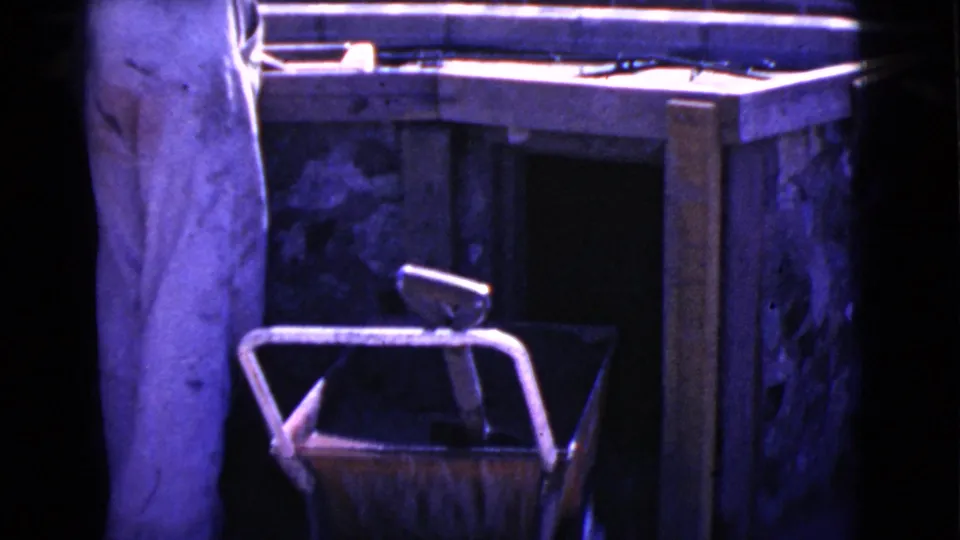 A person in white coveralls stands near a wooden work surface in the 1968 Cottonwood, Arizona home-movie footage.