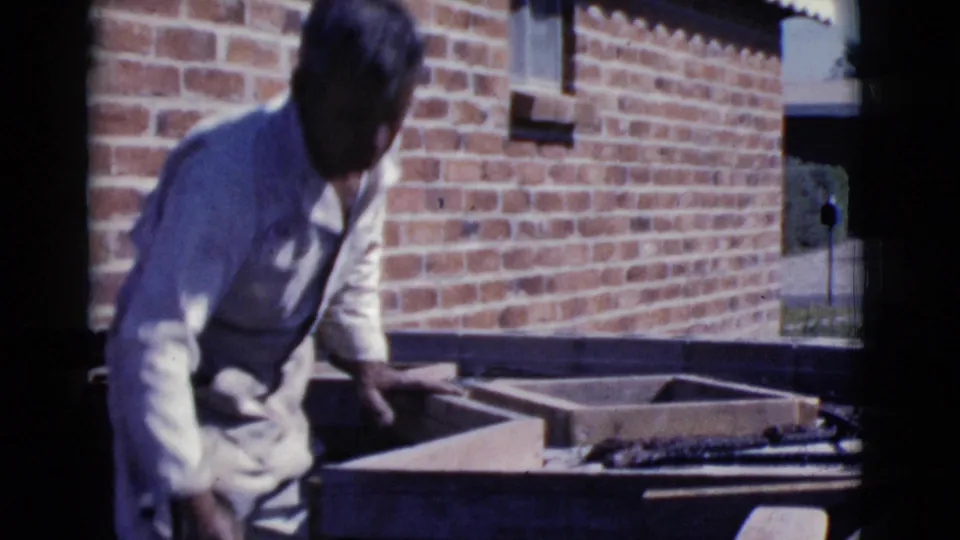 A man leans over a wooden form with mortar and masonry pieces, filmed outdoors in Cottonwood, Arizona in 1968.