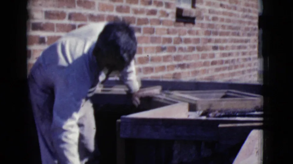 In Cottonwood, Arizona, 1968, a man in white work clothes bends near a mortar tray at an outdoor brick construction area.