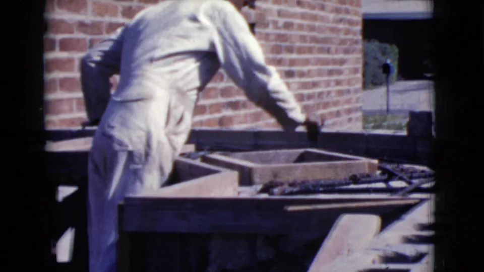 A white-clothed worker reaches over a mortar or cement tray while working beside a red brick wall in the 1968 Cottonwood clip.