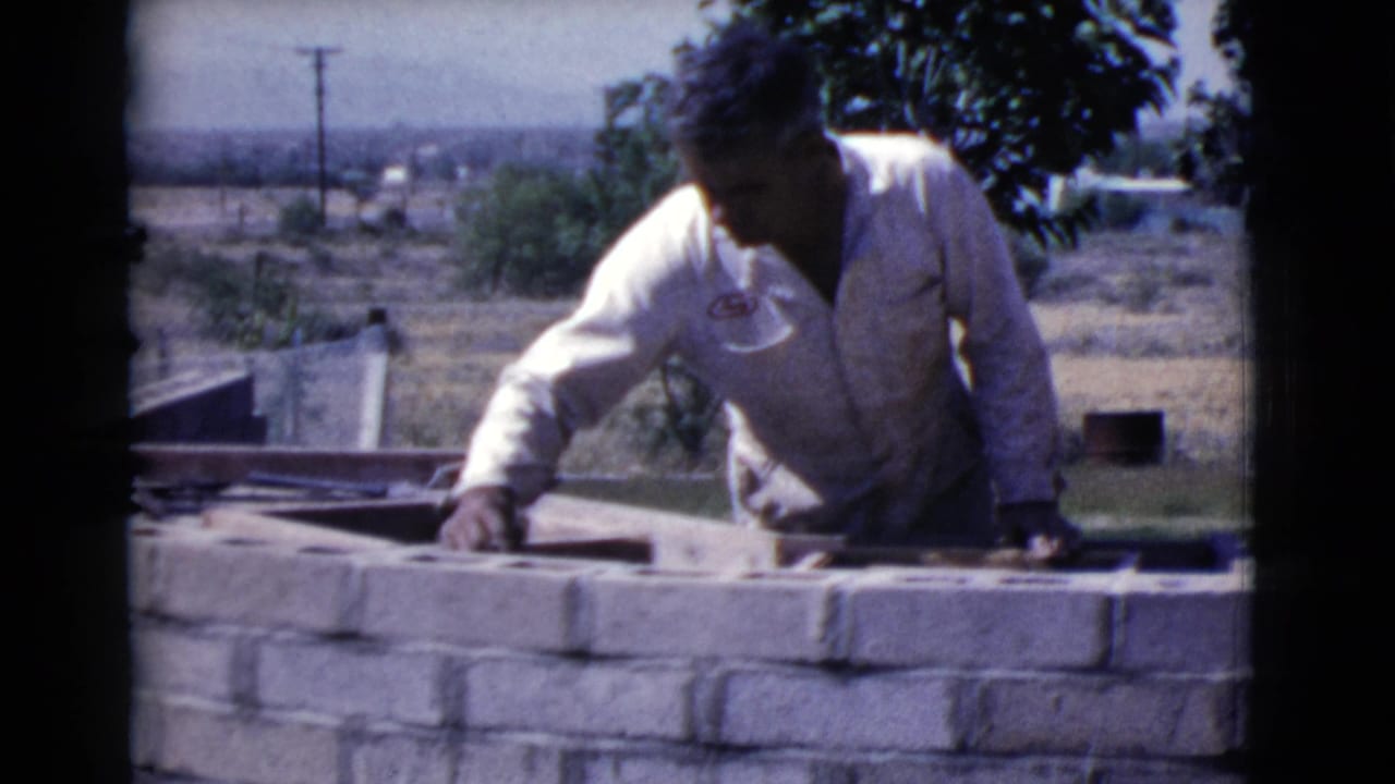 Man in a white work shirt laying concrete blocks outdoors.