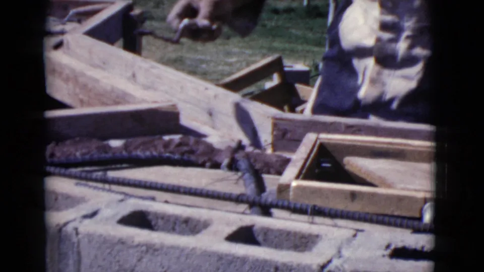The man continues wall construction beside wooden forms, rebar, and concrete blocks in the 1968 Cottonwood home-movie footage.