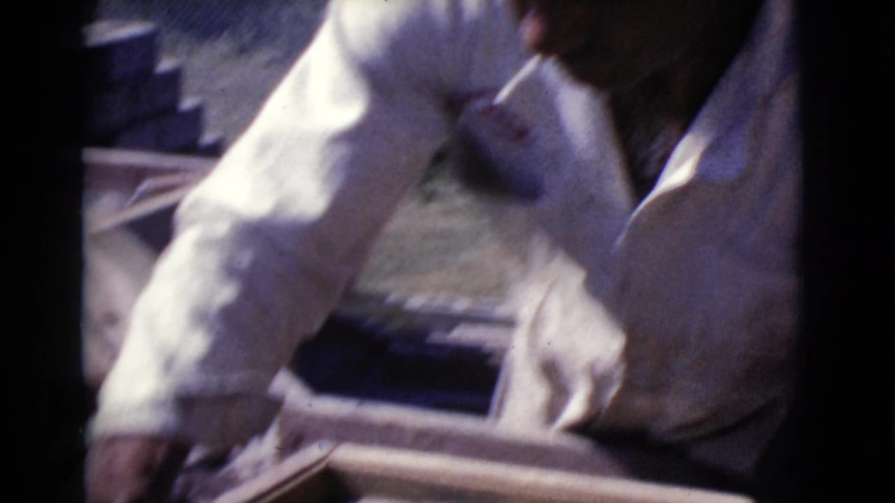 Man in a white shirt working over wooden construction forms outdoors.