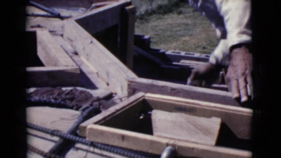 A close 8mm view shows hands working beside wooden forms, rebar, and a tool during a 1968 Arizona construction project.