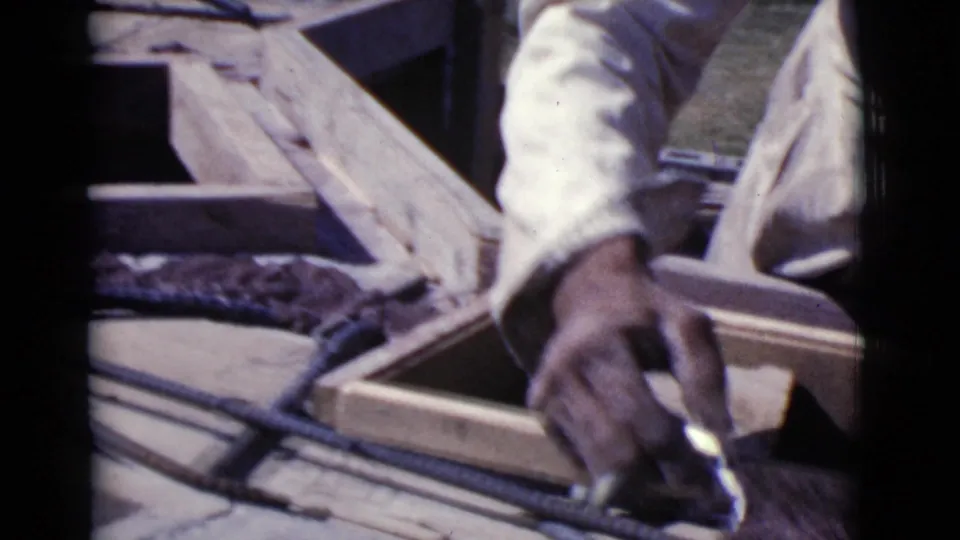 A worker's hand uses a small tool beside wooden forms and rebar in close-up 1968 Cottonwood masonry footage.