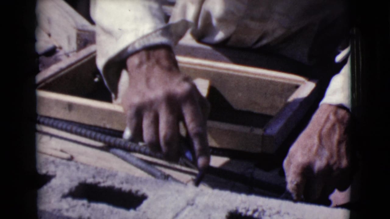 Worker's hands position rebar beside hollow concrete blocks and wood forms.