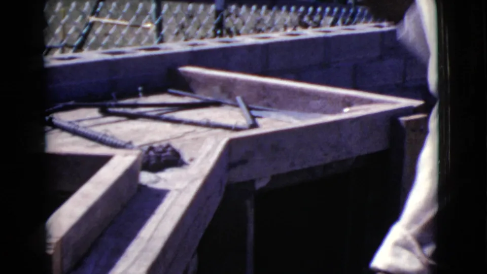 The wooden frame and rebar remain in view as the worker stands partly outside the frame at the outdoor Cottonwood work site.