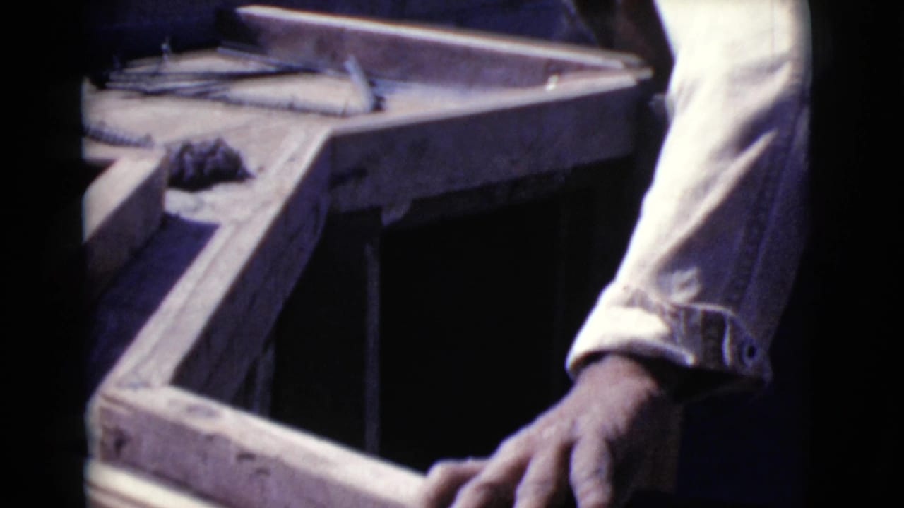 Worker’s hand beside wooden formwork and rebar at an outdoor construction site.