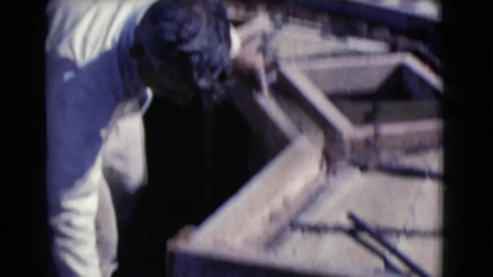 The man leans into the frame while spreading wet mud grout across a wooden form in the 1968 Arizona yard work scene.
