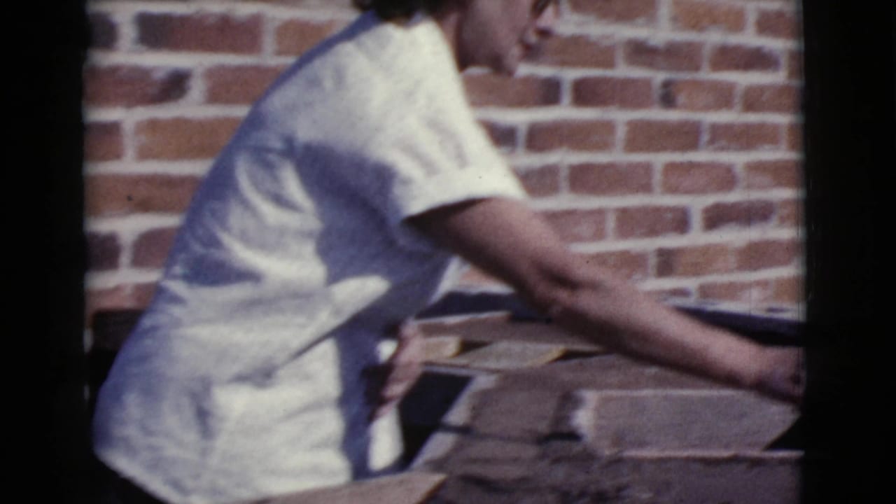 Woman in a light shirt leans over a ledge beside a red brick wall.