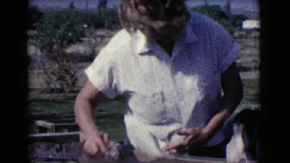 The woman handles a trowel and material near an outdoor yard, continuing the 1968 Cottonwood, Arizona repair or cement work scene.