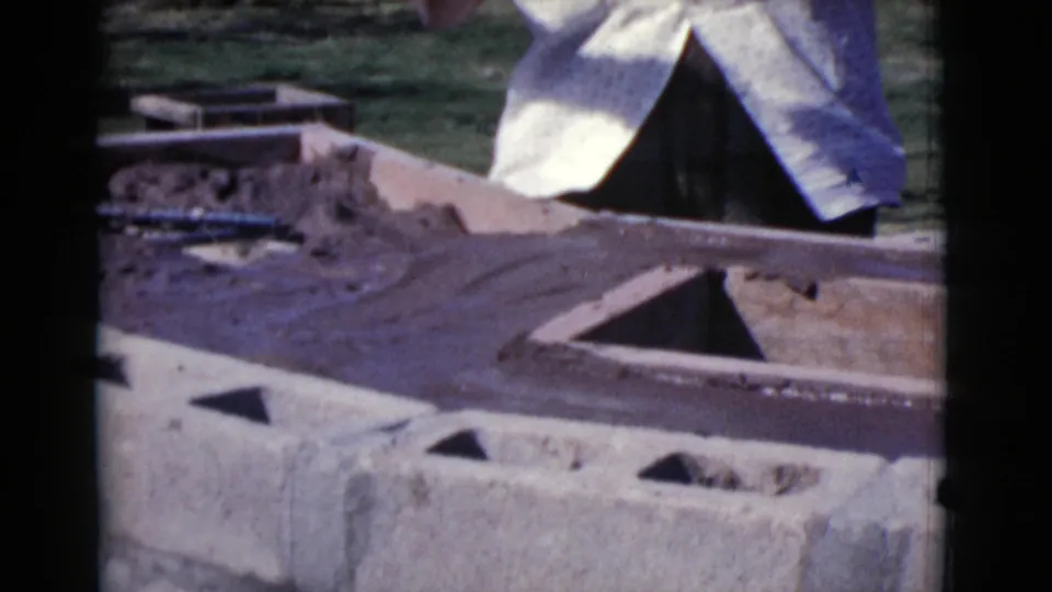 Fresh mortar is spread along a backyard concrete block wall, with the woman partly visible behind the work surface.