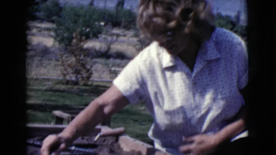 Woman in a white patterned shirt works over a wooden project in a sunny Cottonwood, Arizona yard in 1968.