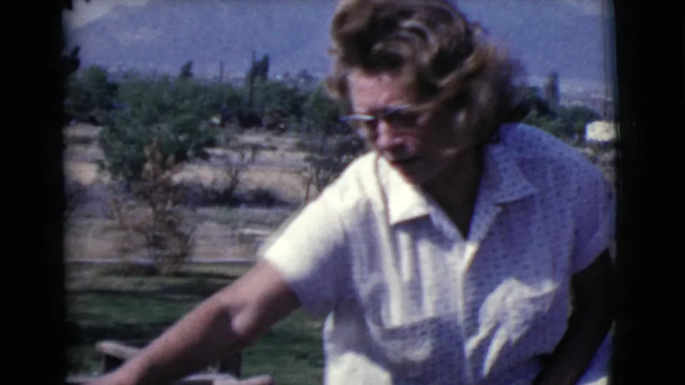 Woman wearing glasses and a white shirt reaches toward a wooden outdoor project in 1968 Cottonwood, Arizona footage.