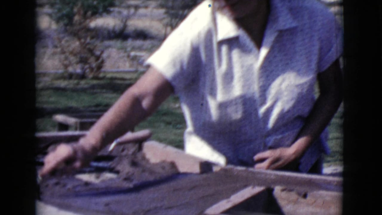 Adult in a white shirt works by a stone or concrete outdoor structure.