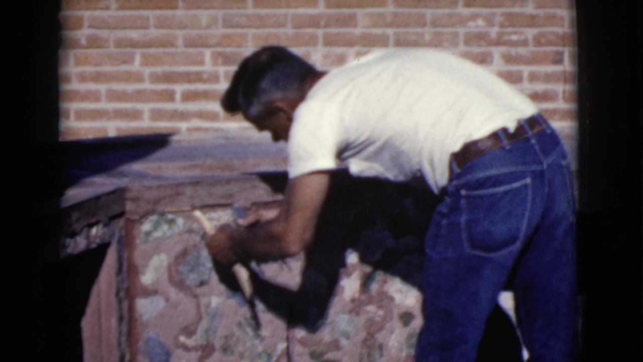 Man bends over a stone fireplace while working with a hand tool.