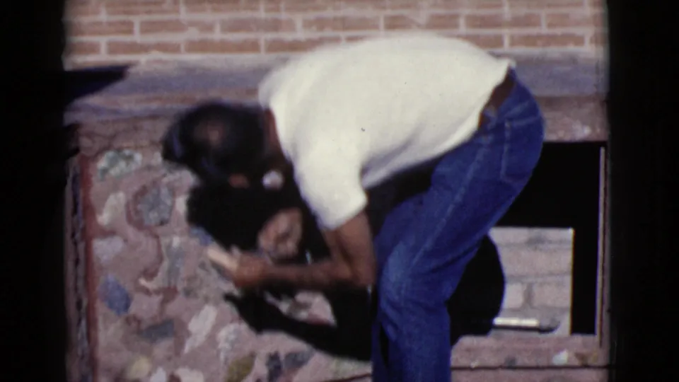 The man bends over the stone fireplace, partly obscuring the work area, as the home-movie footage ends.