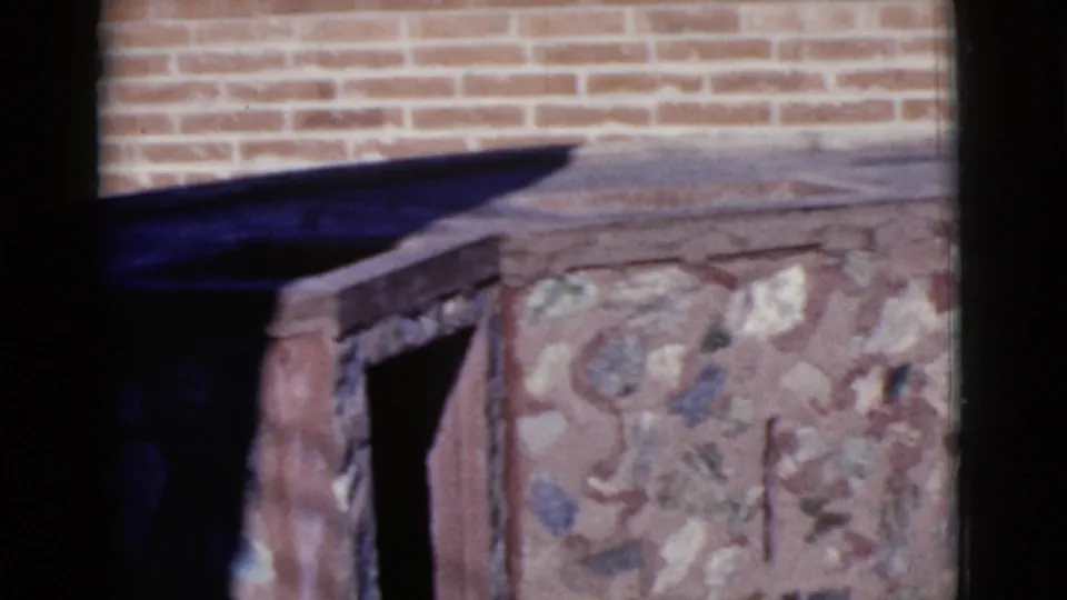 The frame centers on the stone and brick patio structure in the 1968 Cottonwood home-movie scene, with the worker mostly out of view.