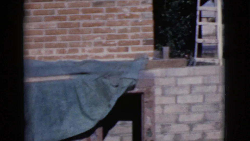 A Cottonwood yard scene shows brickwork, a draped green tarp, and a ladder near a partly built or repaired structure.