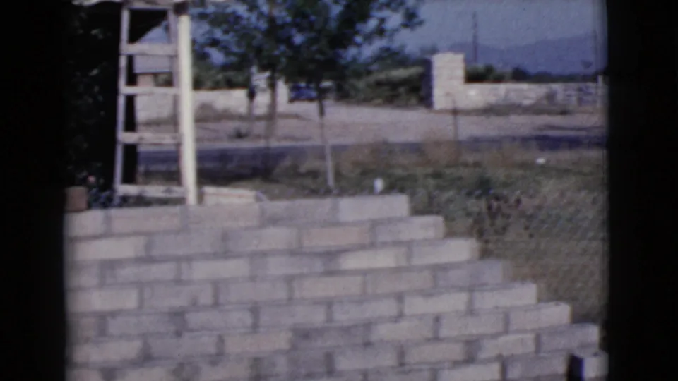 The 1968 Cottonwood home-movie frame shows a low brick wall, ladder, trees, and open yard space beyond the work area.