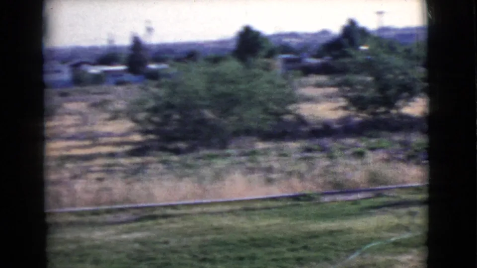 During the 1968 Cottonwood, Arizona pan, the frame shows motion-blurred lawn, field, bushy trees, distant houses, and utility poles.