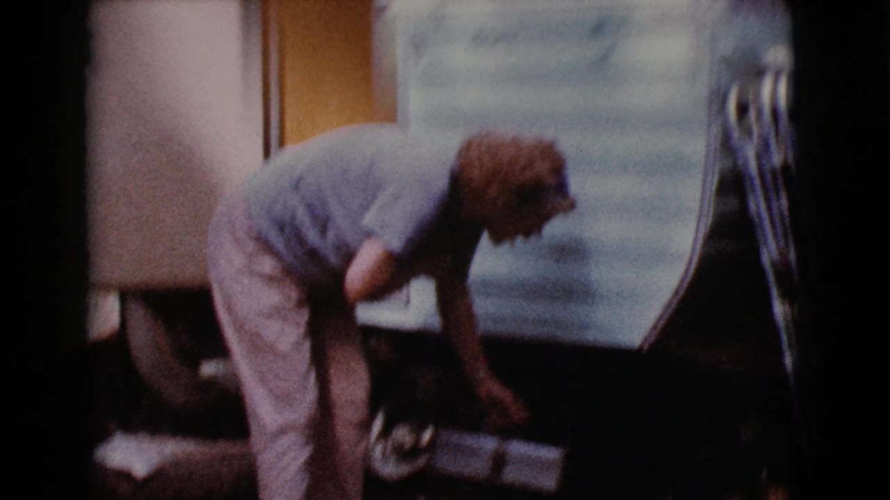 Older woman bending beside a light vintage trailer near under-trailer storage.