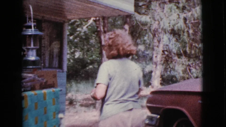 In Cottonwood, Arizona home-movie footage from 1968, a woman stands near a trailer porch and hanging lantern beside trees.