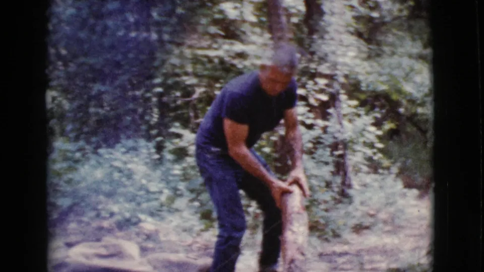 The man handles a piece of firewood in the wooded campsite, captured in grainy 1968 8mm footage from Cottonwood, Arizona.
