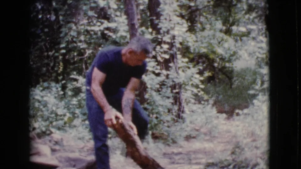 In Cottonwood, Arizona in 1968, an adult man bends over a cut log among trees and brush while working outdoors.