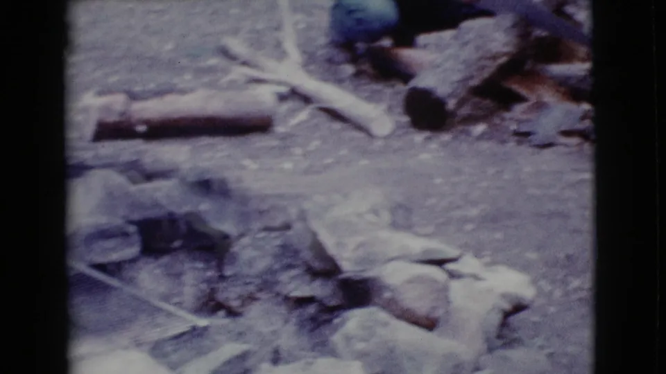 A Cottonwood campsite view shows firewood, branches, stones, and a partially visible adult near the work area.