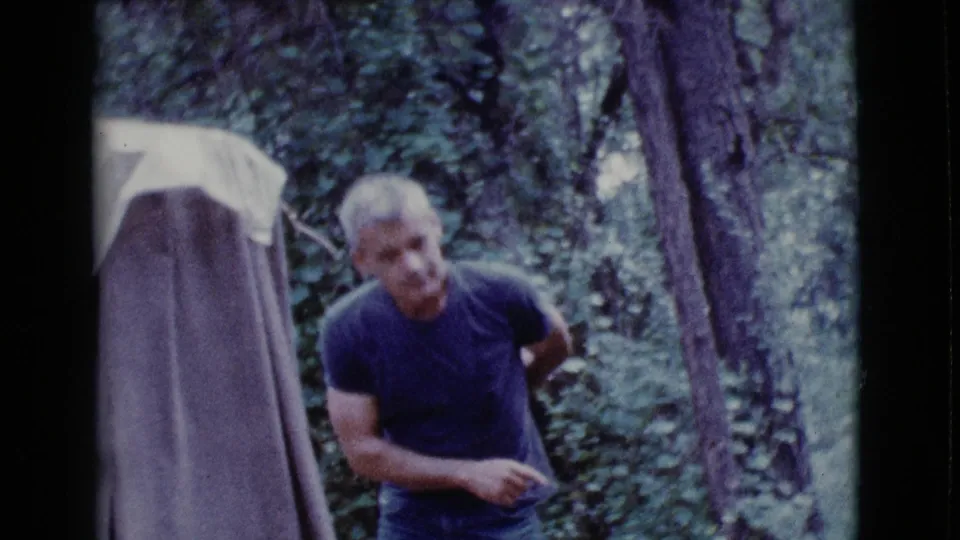The man stands beside the brown tent in the wooded Cottonwood, Arizona setting, turning toward the camera.